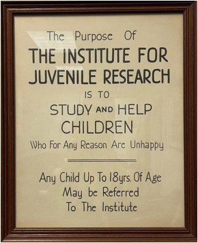 An old, framed sign reading: "The Purpose Of THE INSTITUTE FOR JUVENILE RESEARCH IS TO STUDY and HELP CHILDREN Who For Any Reason Are Unhappy | Any Child Up to 18yrs Of Age May be Referred To The Institute"